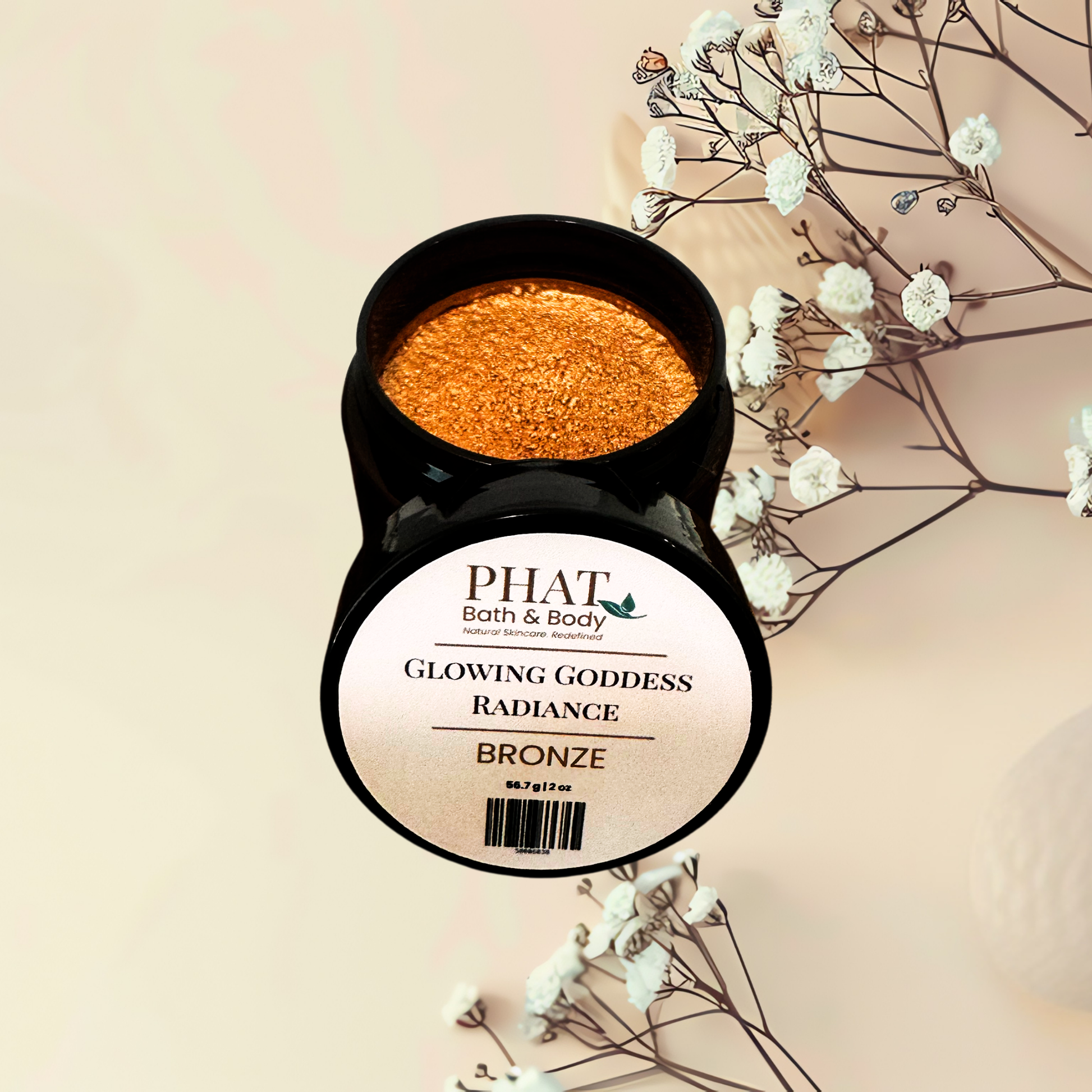 An open black jar of PHAT Bath & Body 'Glowing Goddess Radiance' body powder in the shade 'Bronze', showing the sparkling orange-bronze product inside, styled with dried baby's breath flowers on a warm beige background.