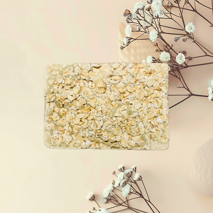Square bar of soap with textured surface on a light pink background with dried flowers.