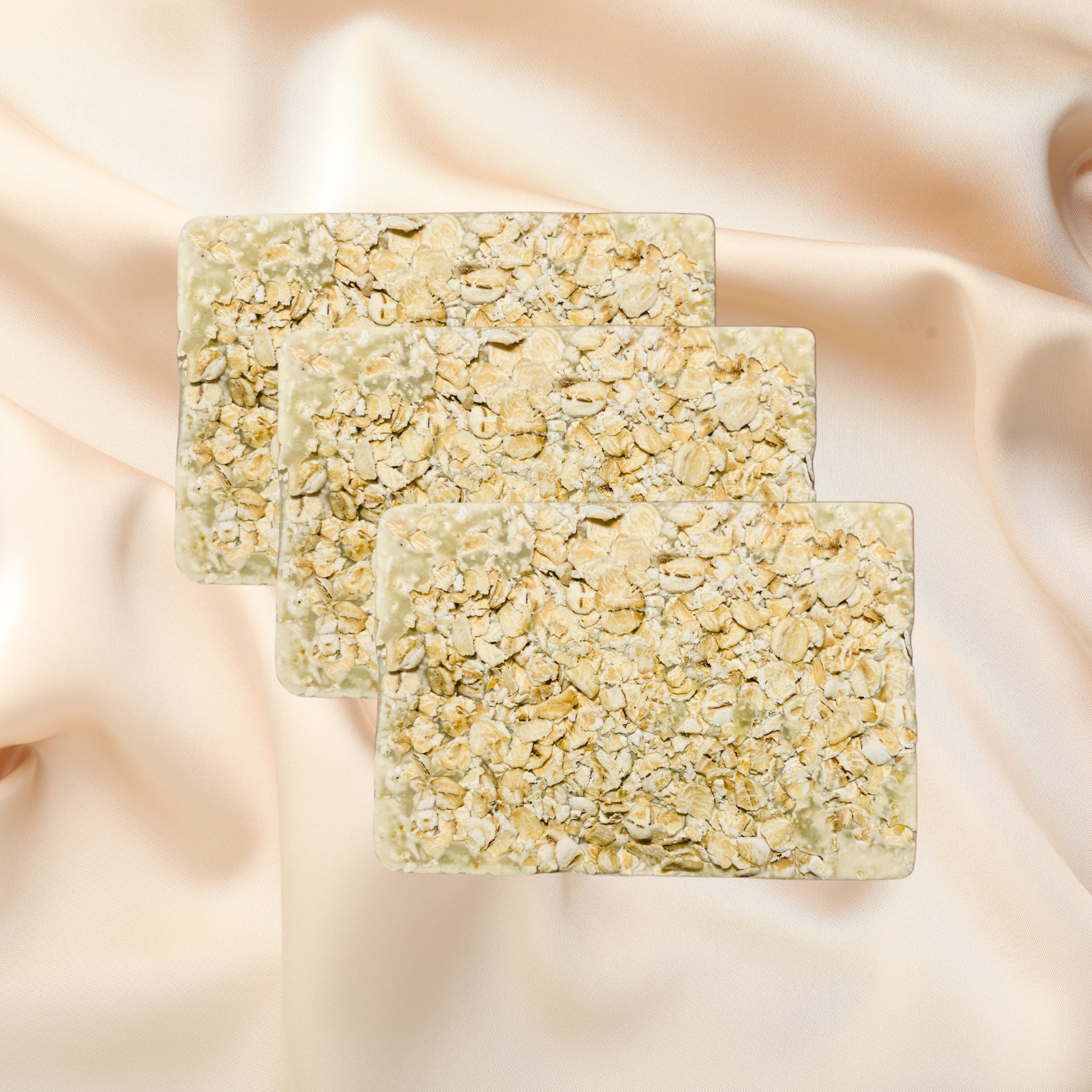 Three square soap bars with a textured surface on a soft pink fabric background
