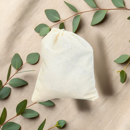White drawstring bag on a beige fabric background with green leaves