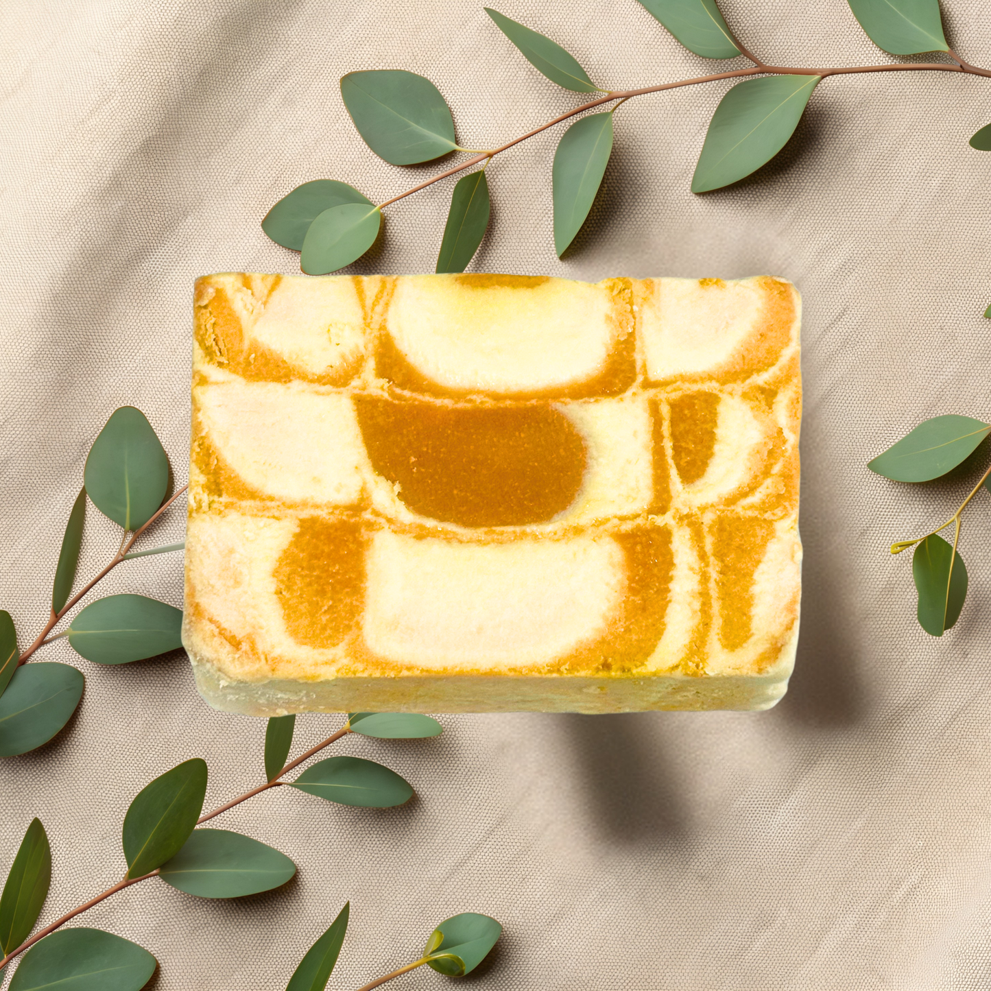 Marble-patterned soap bar with green leaves on a beige fabric background