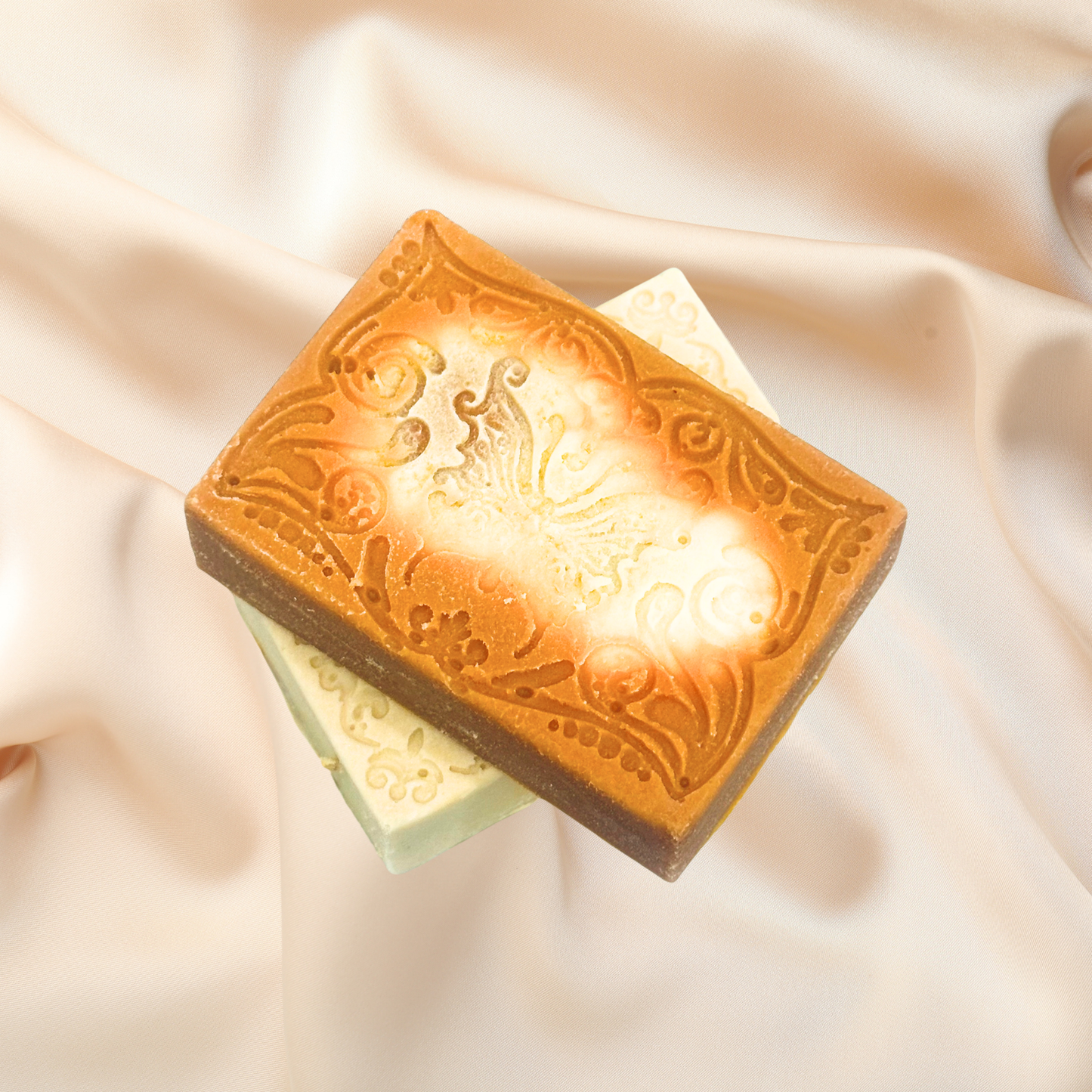 Two soap bars with decorative embossing on a soft fabric background