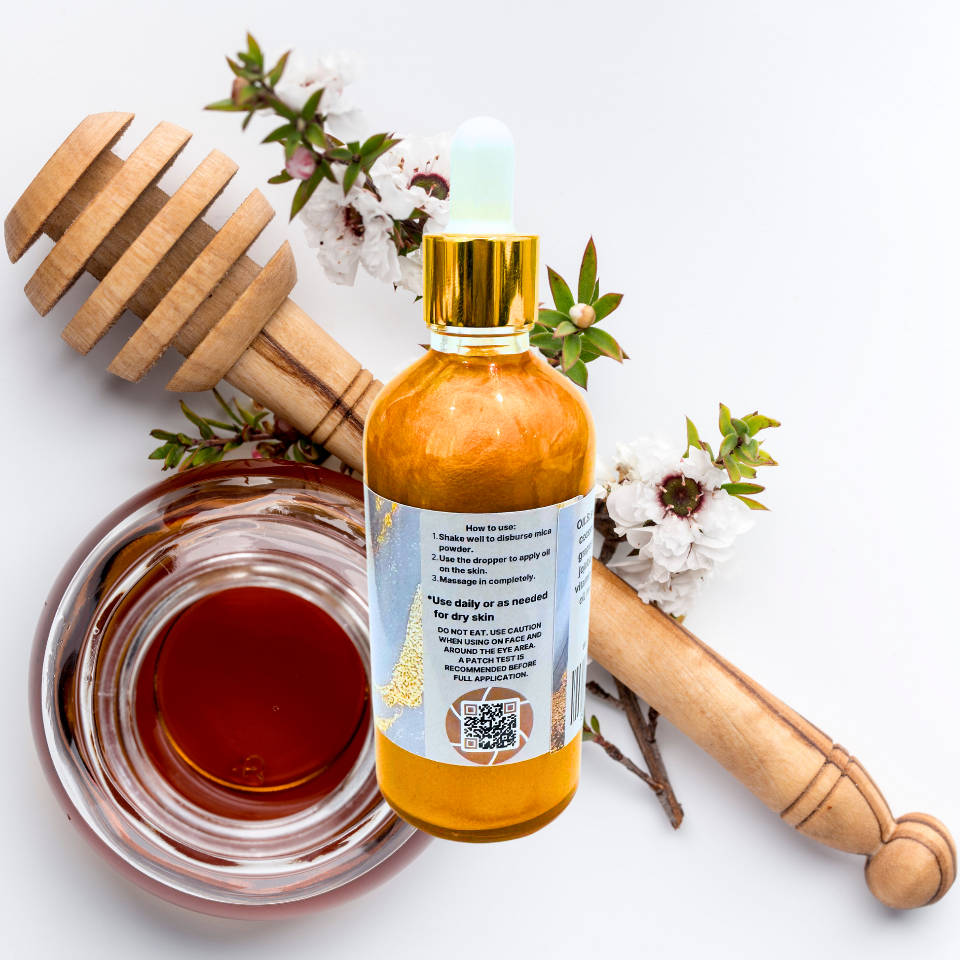 Bottle of shimmer oil with a wooden dipper and flowers on a white background