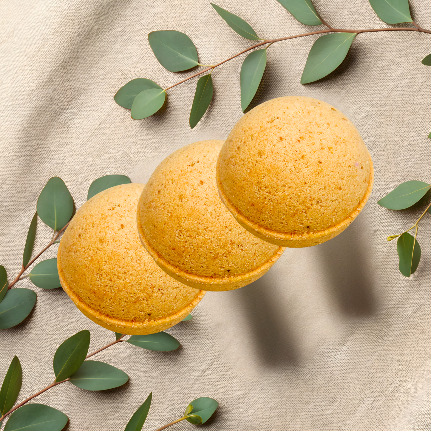 Three yellow bath bombs with green leaves on a beige fabric background