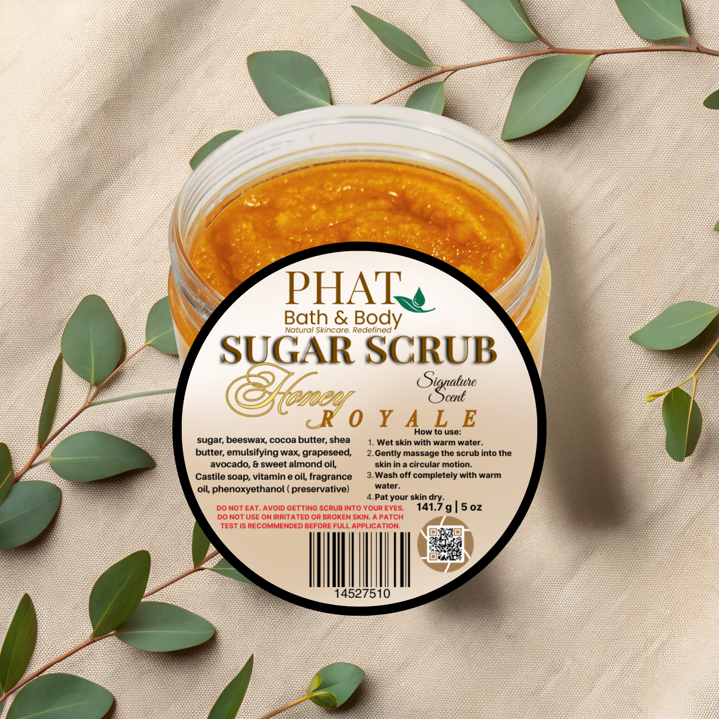 Jar of Phat Bath & Body sugar scrub with honey on a beige fabric background with green leaves.