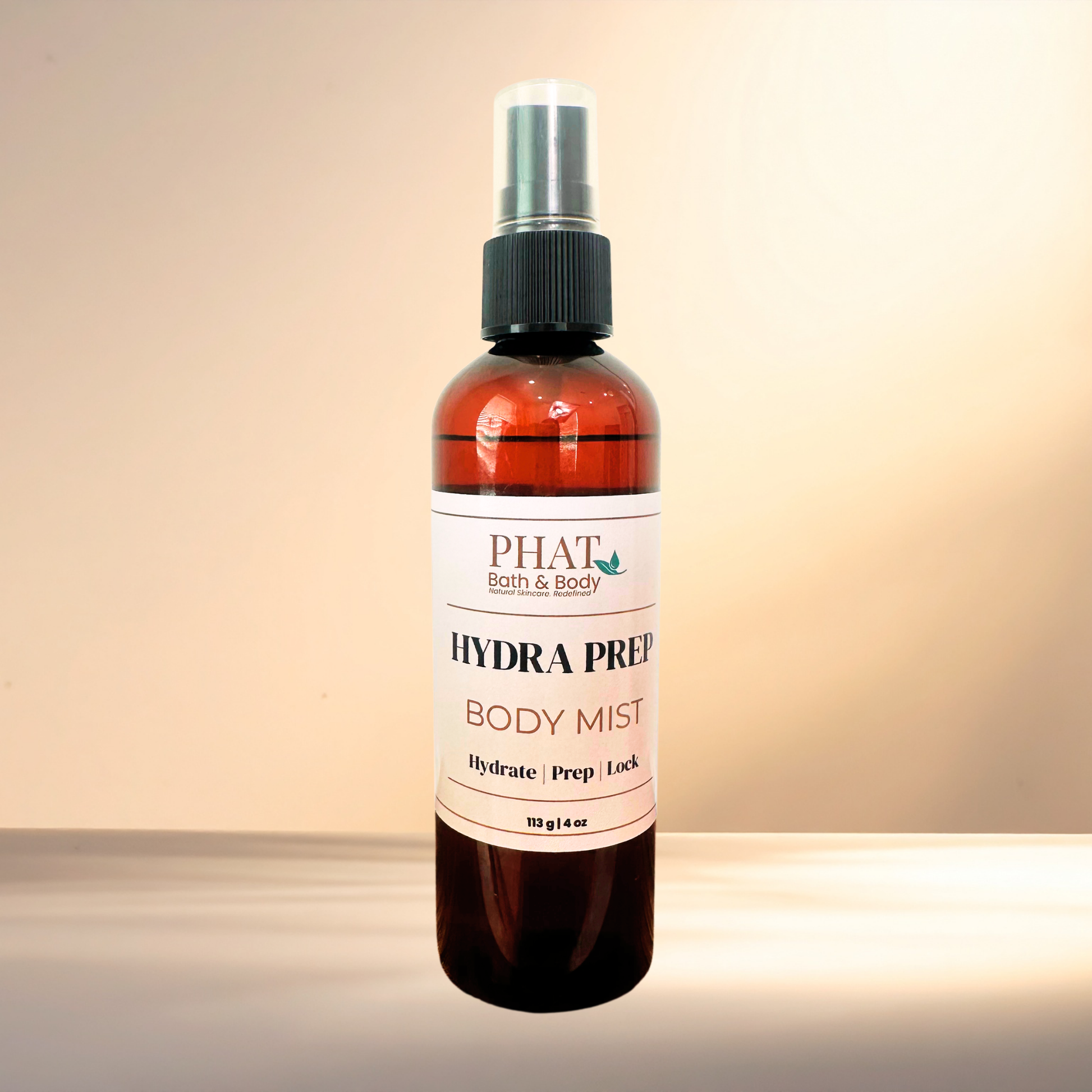 An amber spray bottle of PHAT Bath & Body Hydra Prep Body Mist with a black spray cap and white label, set against a warm beige gradient background.