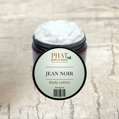 Jar of 'Jean Noir' body lotion from Phat Bath & Body on a beige fabric background with green leaves.