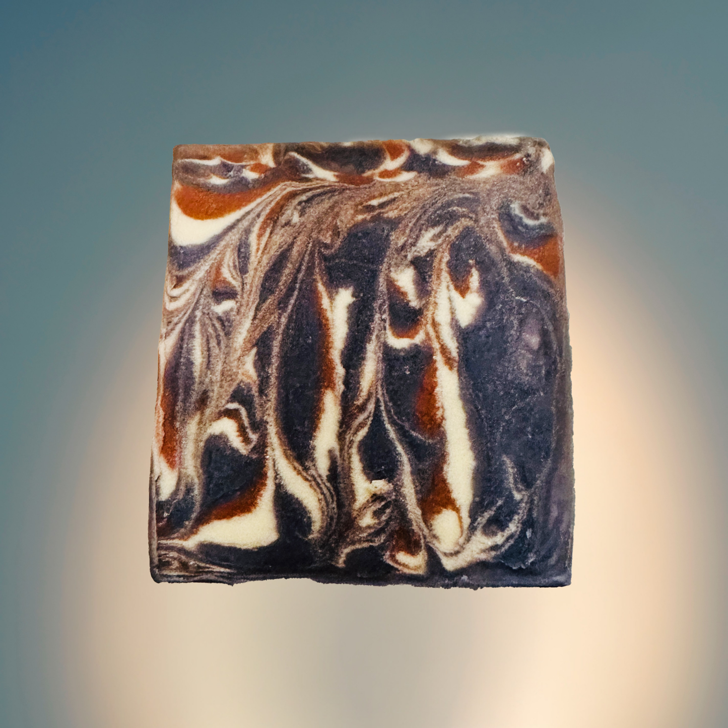 Marbled soap bar with brown, white, and black swirled pattern on a gradient background
