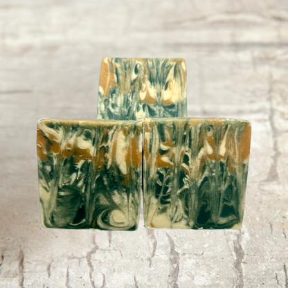 Three marbled soap bars with green and brown hues on a textured beige background