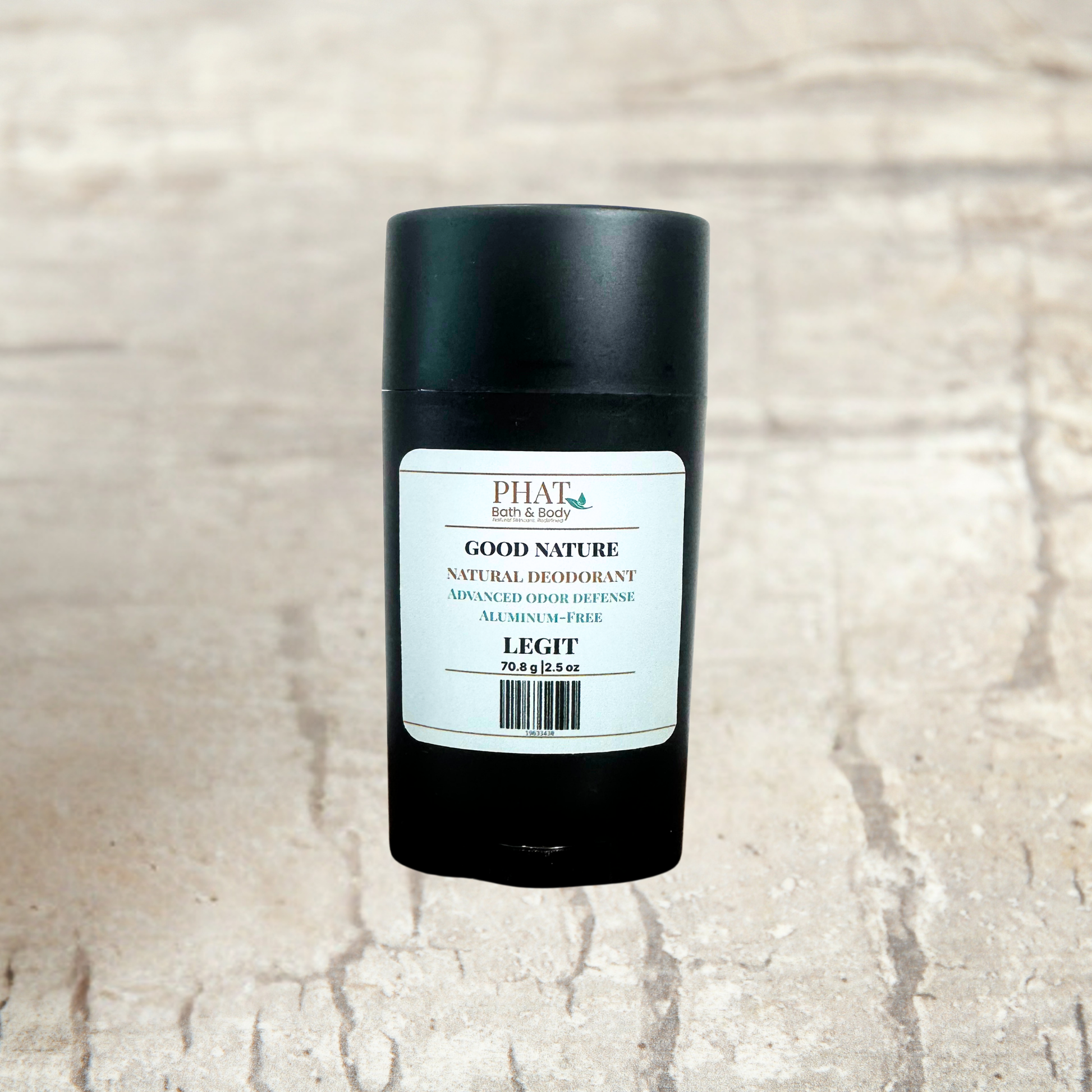 A black cylindrical deodorant stick with a white label reading Good Nature Natural Deodorant, placed on a light textured stone surface.
