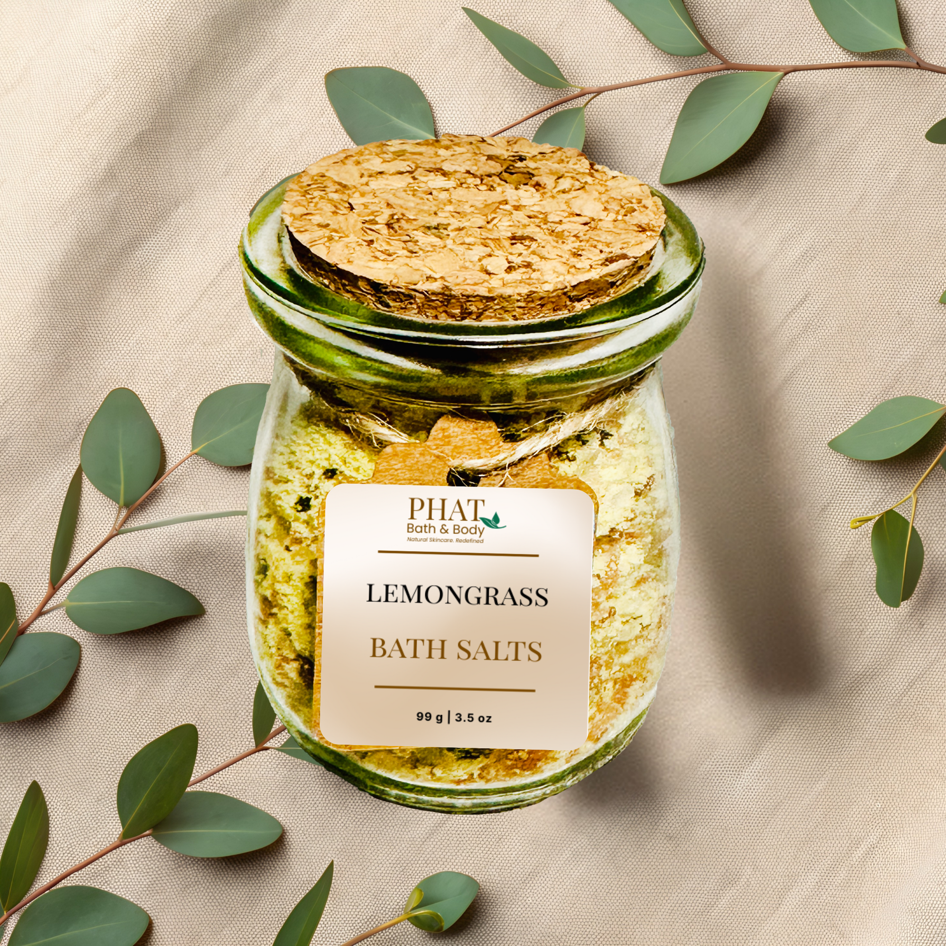 Jar of 'Lemongrass' bath salts with a cork lid on a beige fabric background with eucalyptus leaves.
