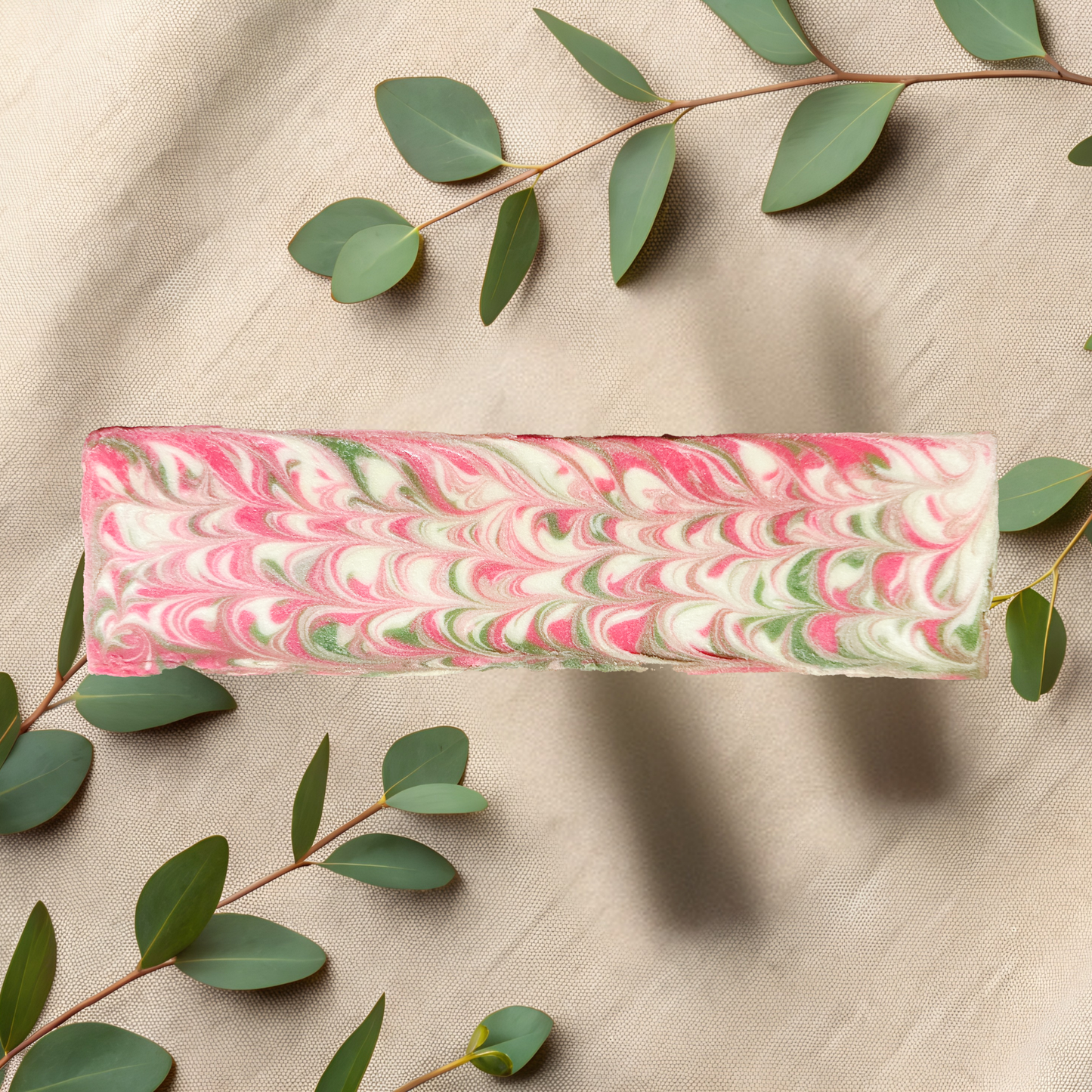 Marbled pink and green soap bar on a beige fabric background with eucalyptus leaves.