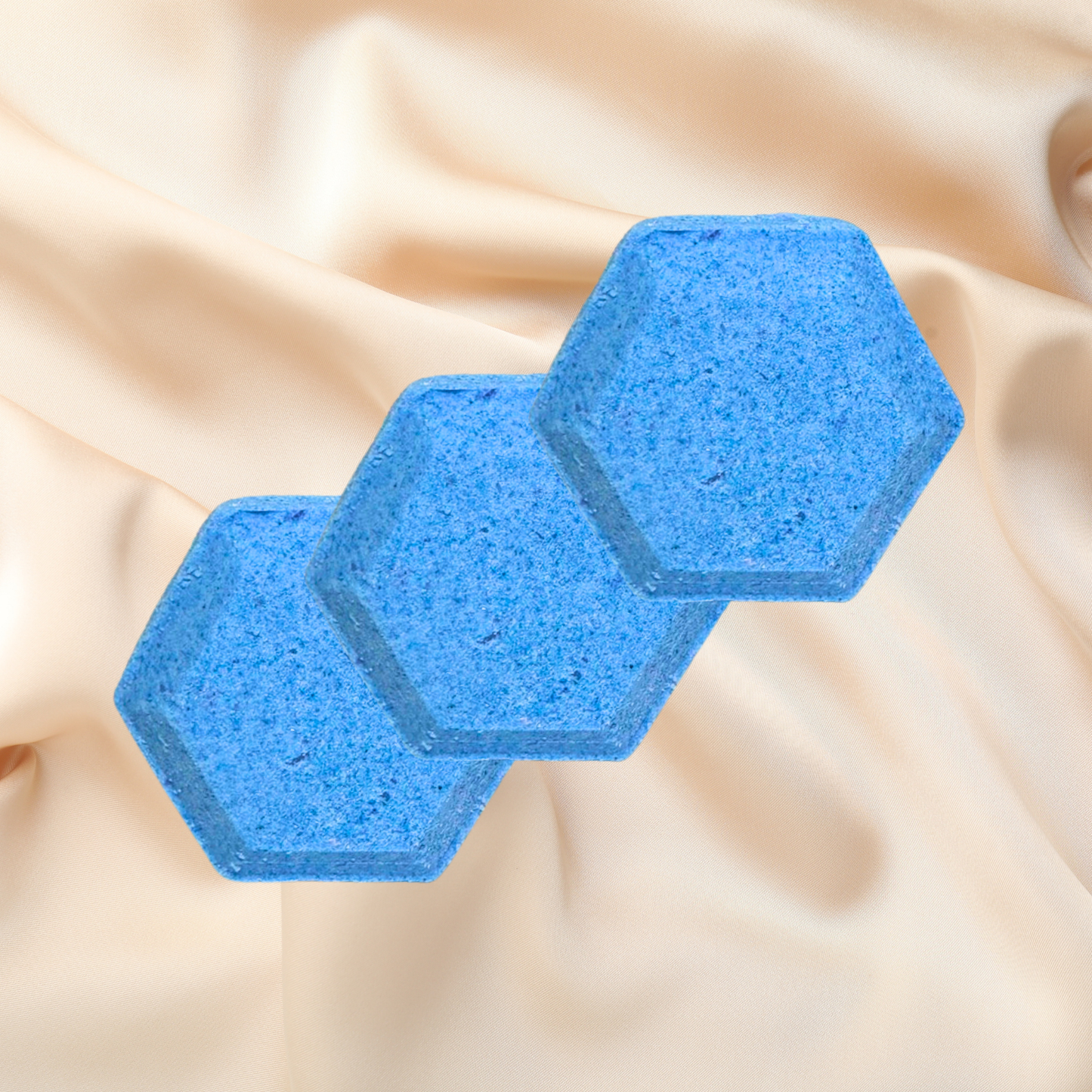 Two blue hexagonal shower bombs on a beige fabric background