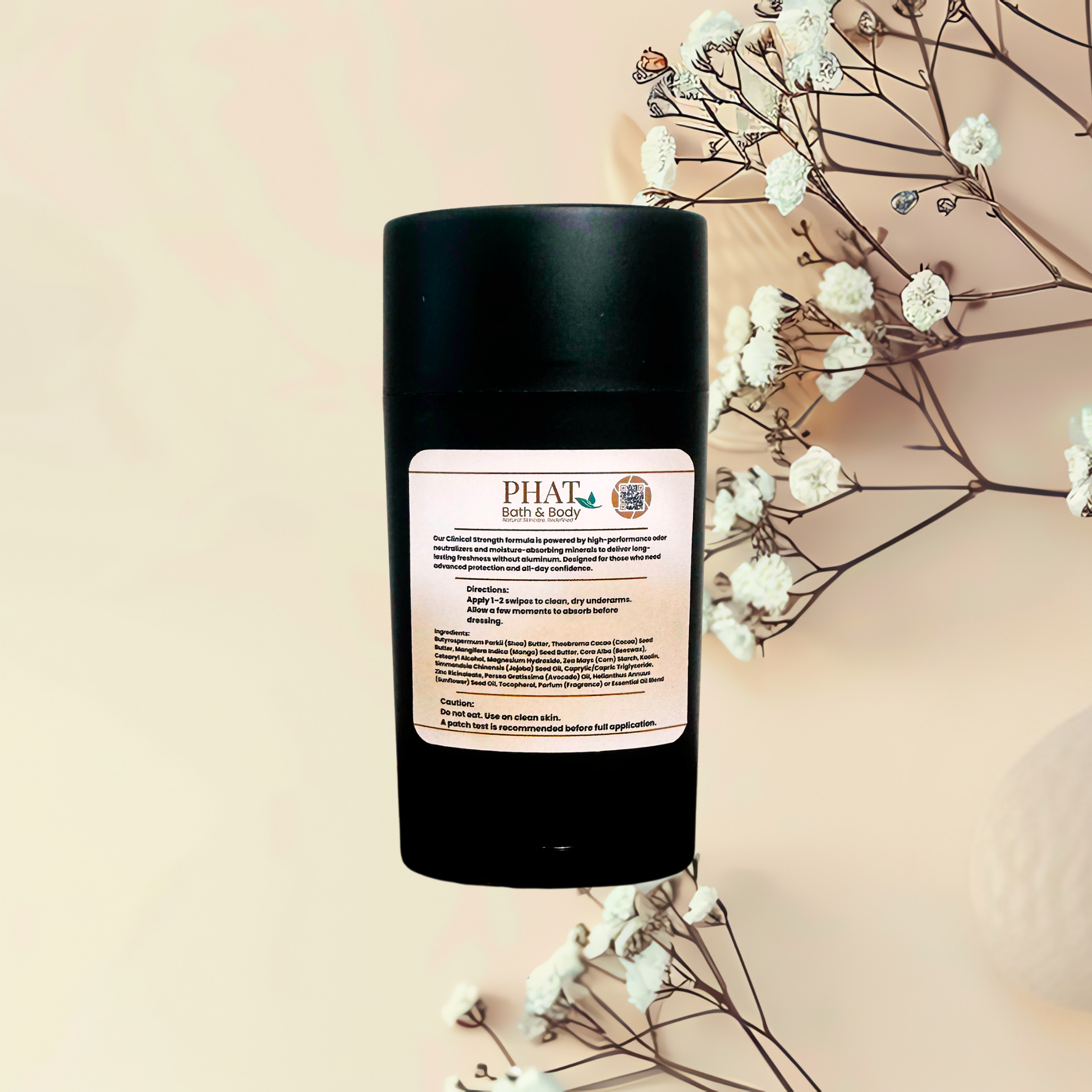 A black cylindrical bottle of PHAT Bath & Body deodorant with a cream-colored label, styled with dried white flowers on a warm beige background.