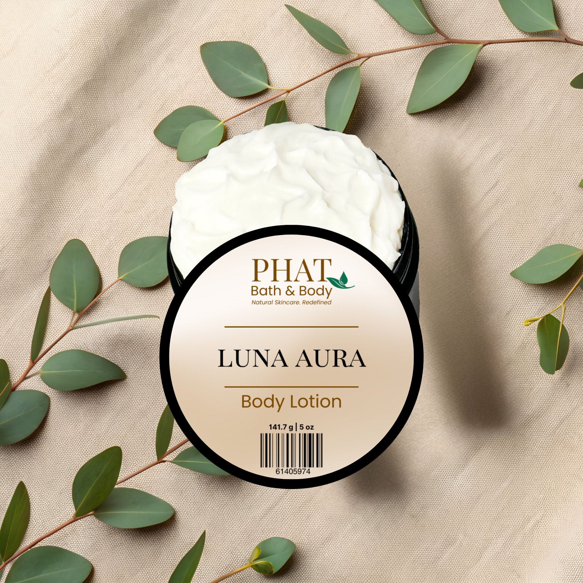 Body lotion jar labeled 'Luna Aura' by PHAT Bath & Body on a beige fabric background with green leaves.