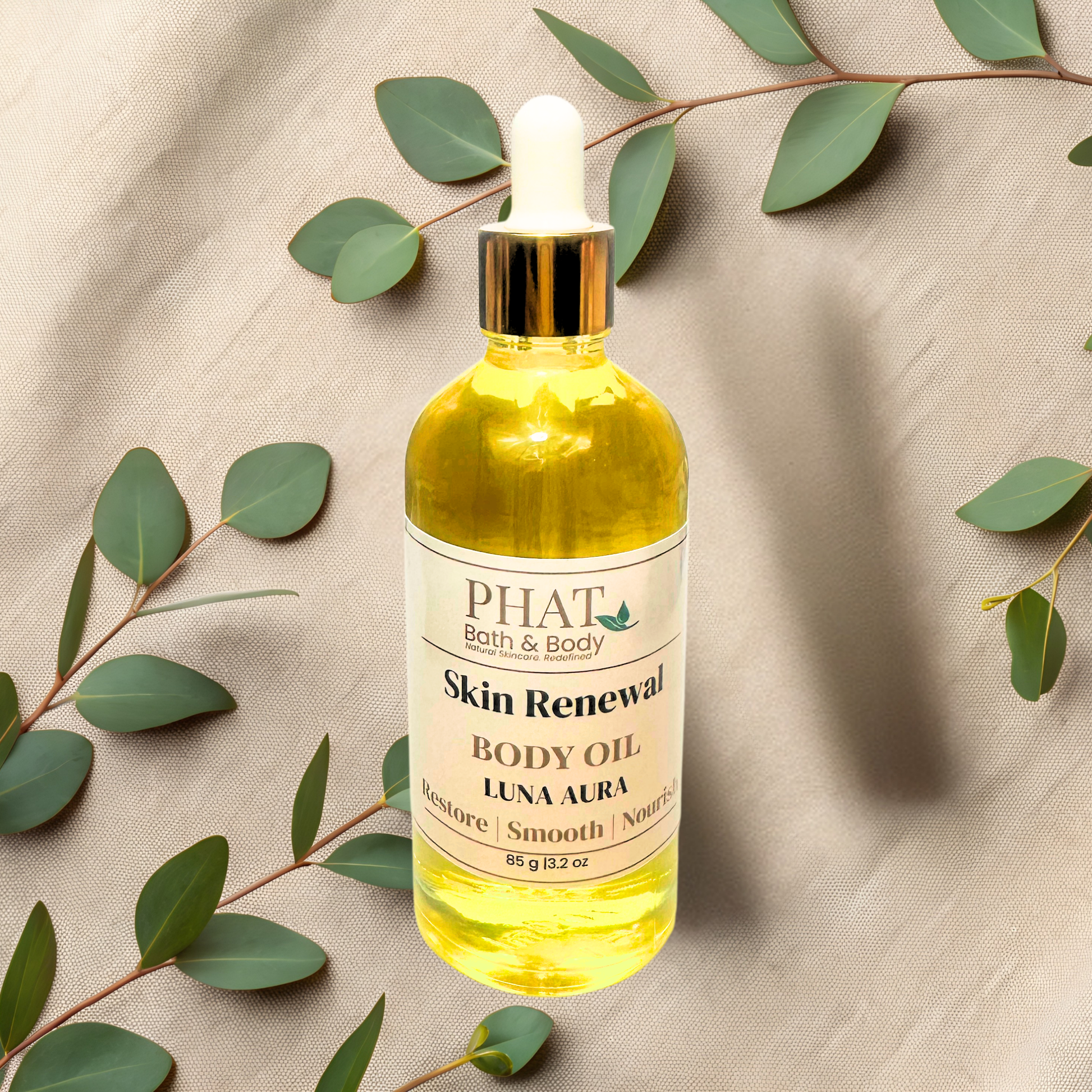 Bottle of PHAT Bath & Body Oil on a beige fabric background with green leaves.