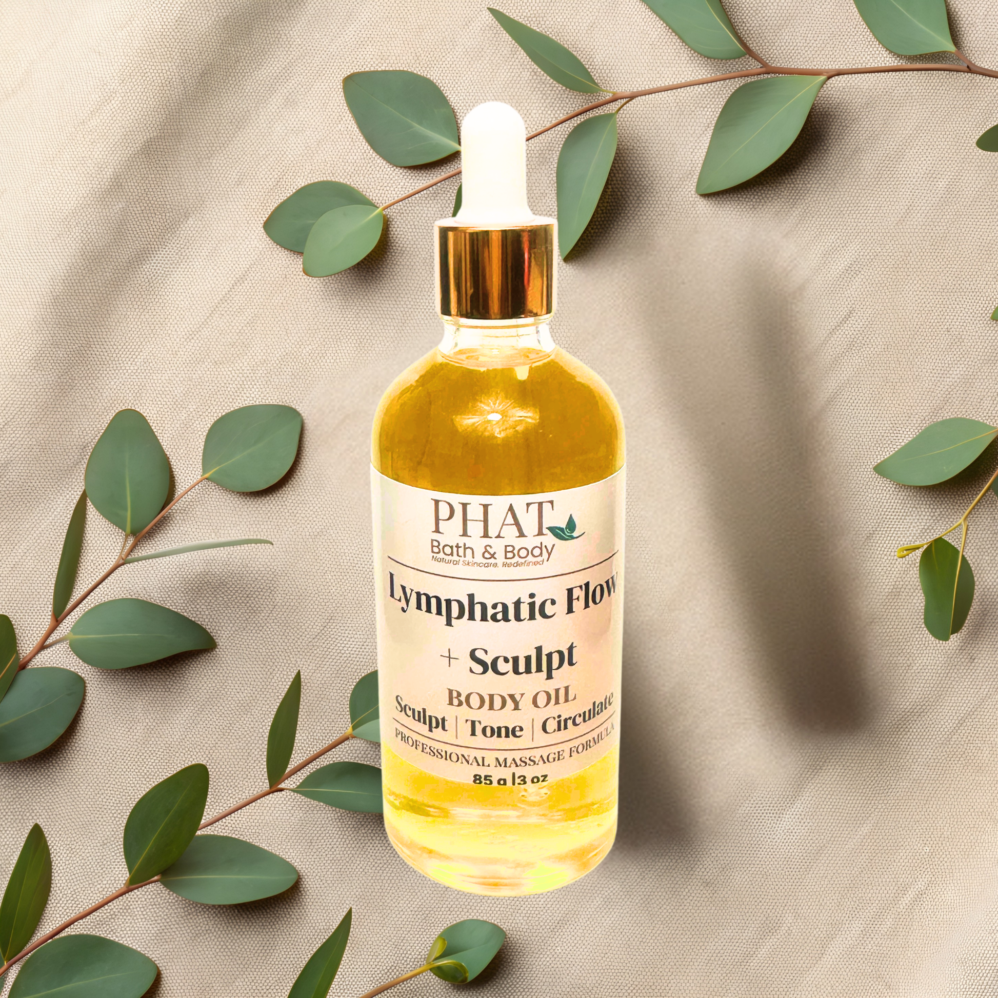 Body oil bottle labeled 'PHAT Bath & Body' with green leaves on a beige fabric background