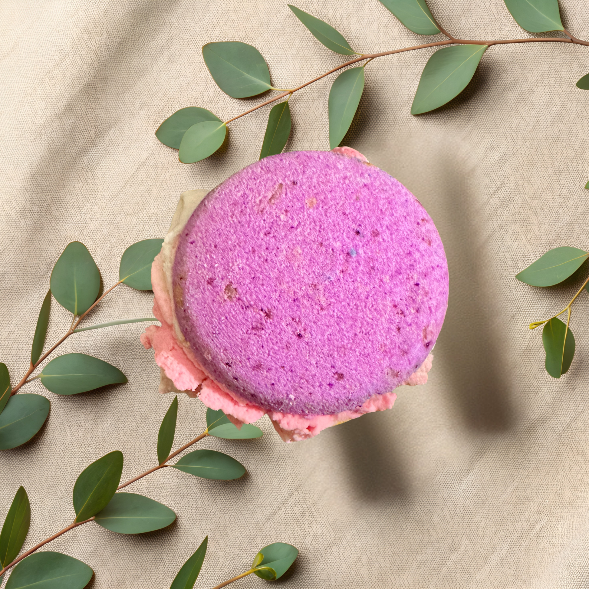 Purple bubble bomb with pink bubble frosting on a beige fabric background with green leaves