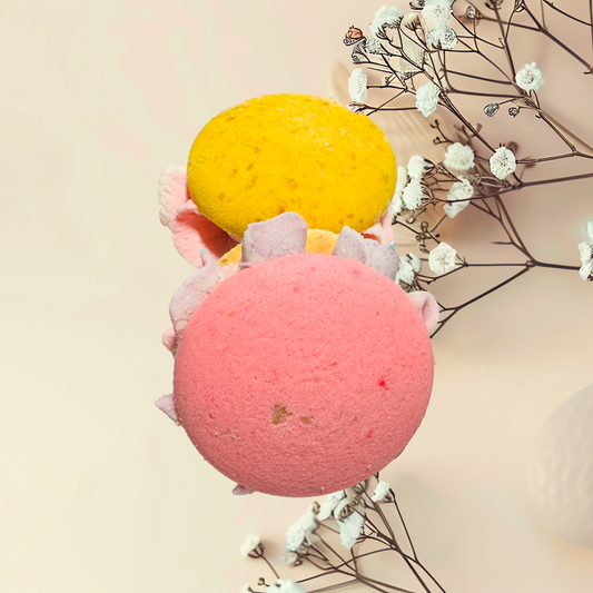 Two bath bombs, one pink and one yellow, with dried flowers on a light background.