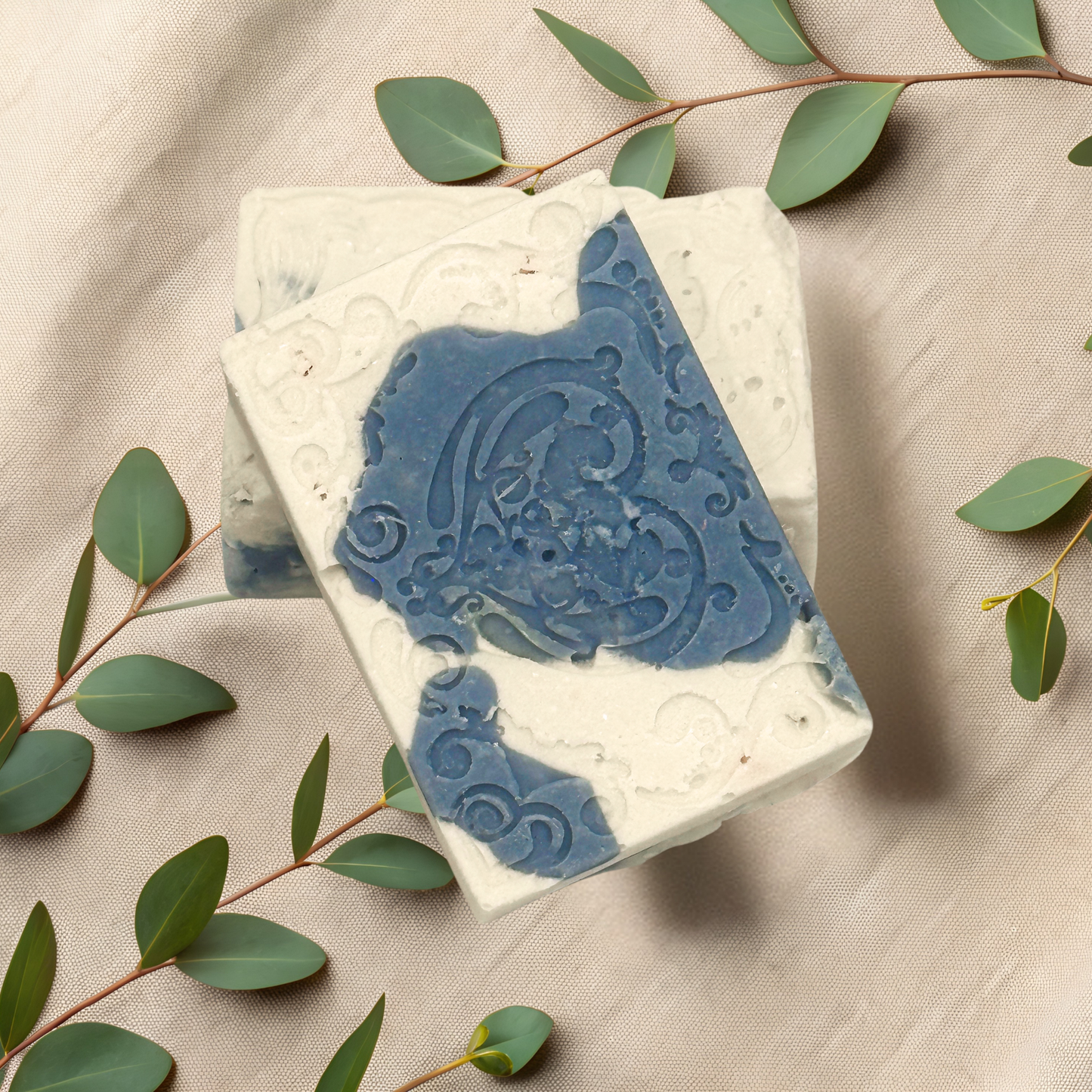 Bar of soap with blue decorative design on a beige fabric background with green leaves.