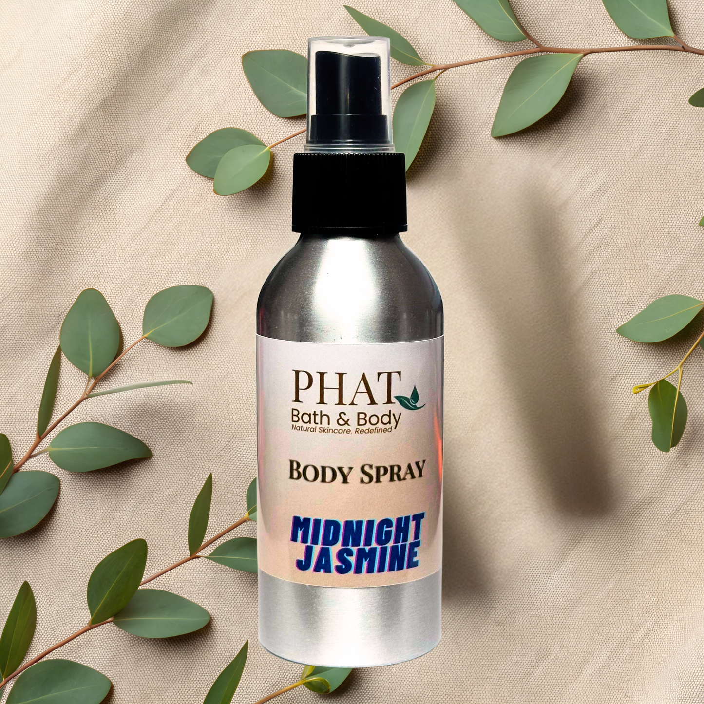 Body spray bottle labeled 'PHAT Bath & Body' with 'Midnight Jasmine' scent on a beige fabric background with green leaves.