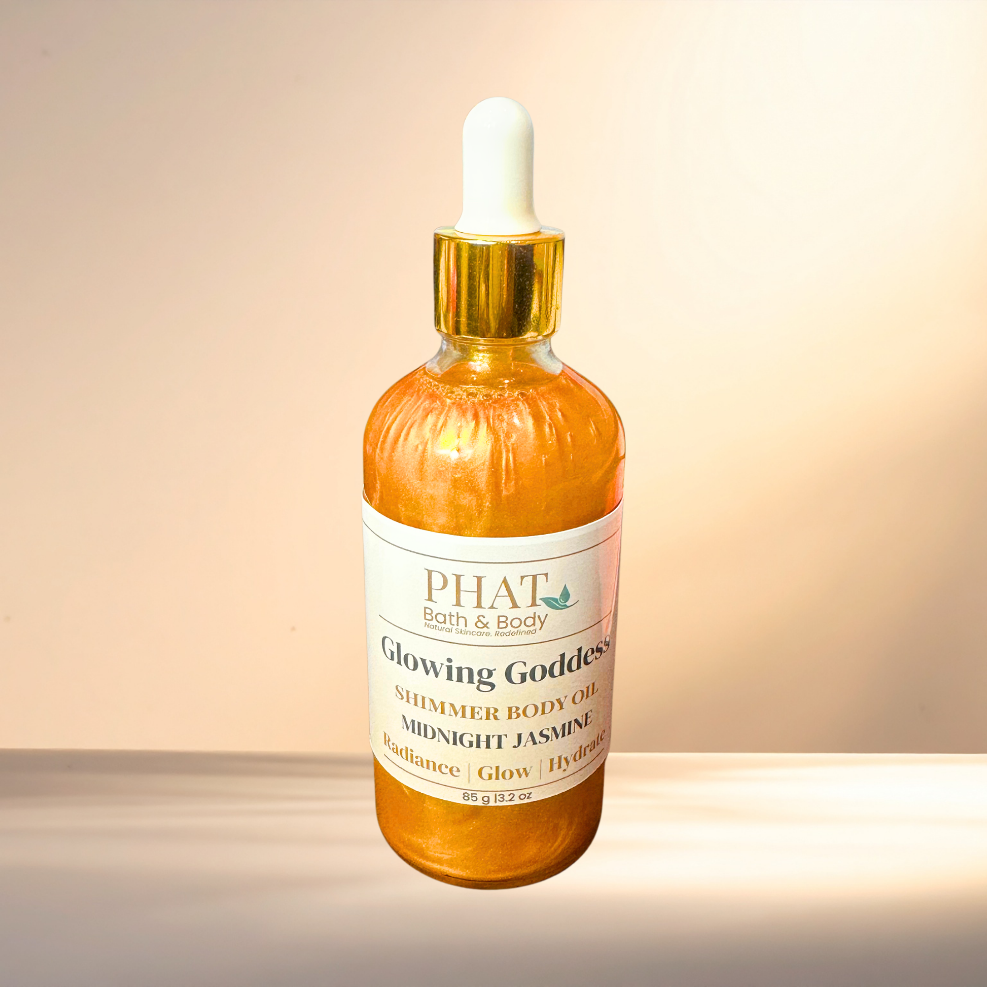 Bottle of 'Glowing Goddess' shimmer body oil from PHAT Bath & Body on a gradient background