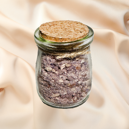 Glass jar with cork lid containing a purple bath salt mix on a beige fabric background