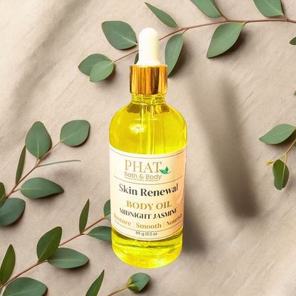 Bottle of Phat Bath & Body Skin Renewal Body Oil with a dropper on a beige fabric background with green leaves.