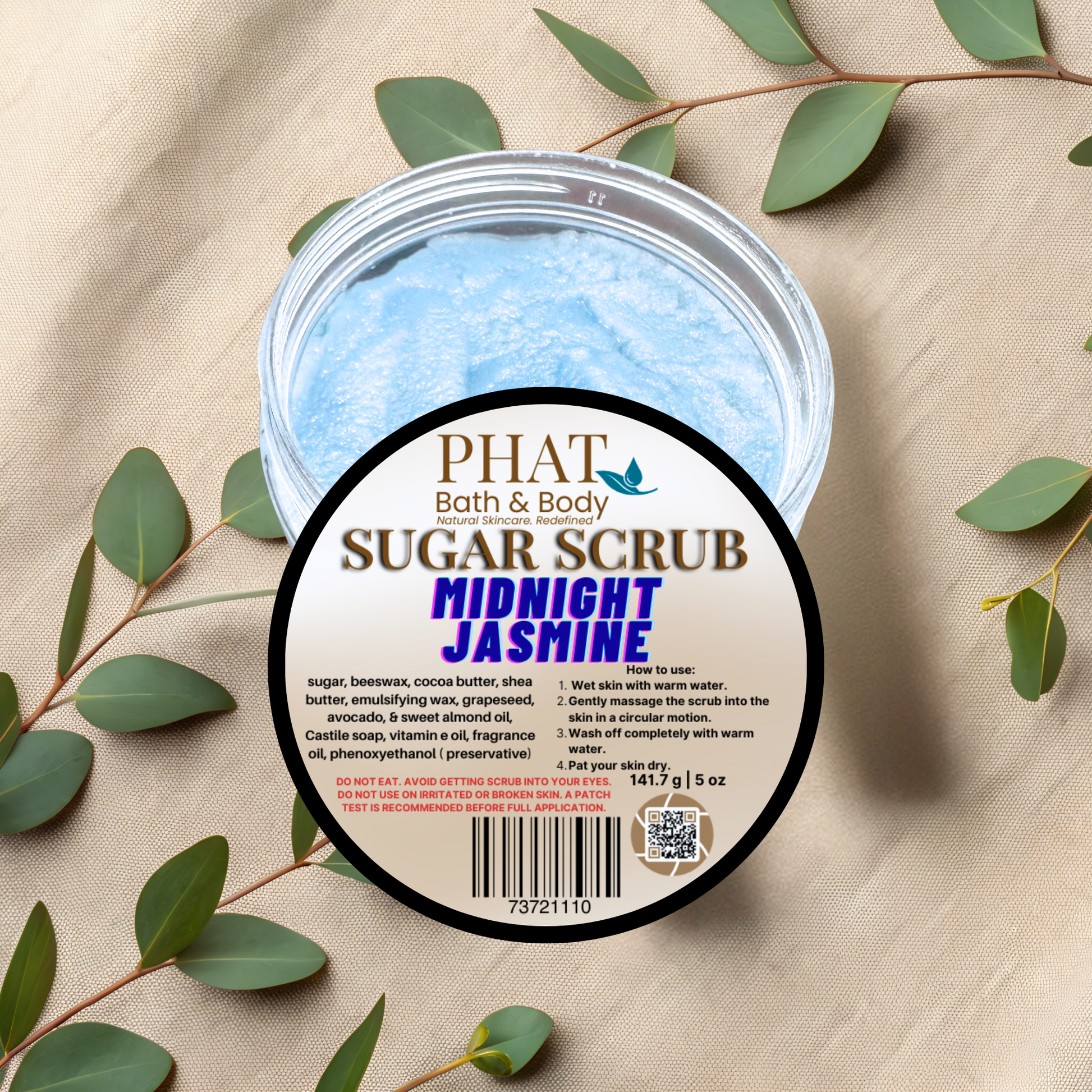 Jar of Phat Bath & Body Sugar Scrub with 'Midnight Jasmine' scent on a beige fabric background with green leaves.