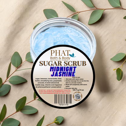 Jar of Phat Bath & Body Sugar Scrub with 'Midnight Jasmine' scent on a beige fabric background with green leaves.