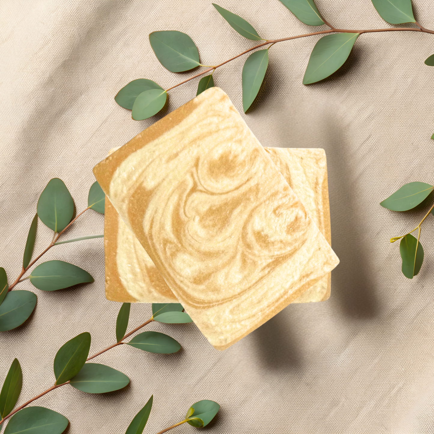 Two soap bars with a swirling pattern on a beige fabric background with green leaves.