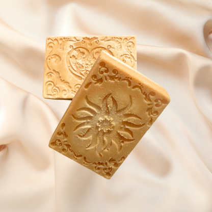 Two square soap bars with decorative patterns on a soft beige fabric background