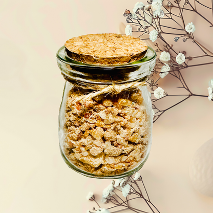 Glass jar with cork lid containing a bath salts, surrounded by delicate white flowers on a light background