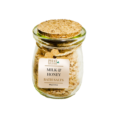 Glass jar of milk and honey bath salts with a cork lid on a white background