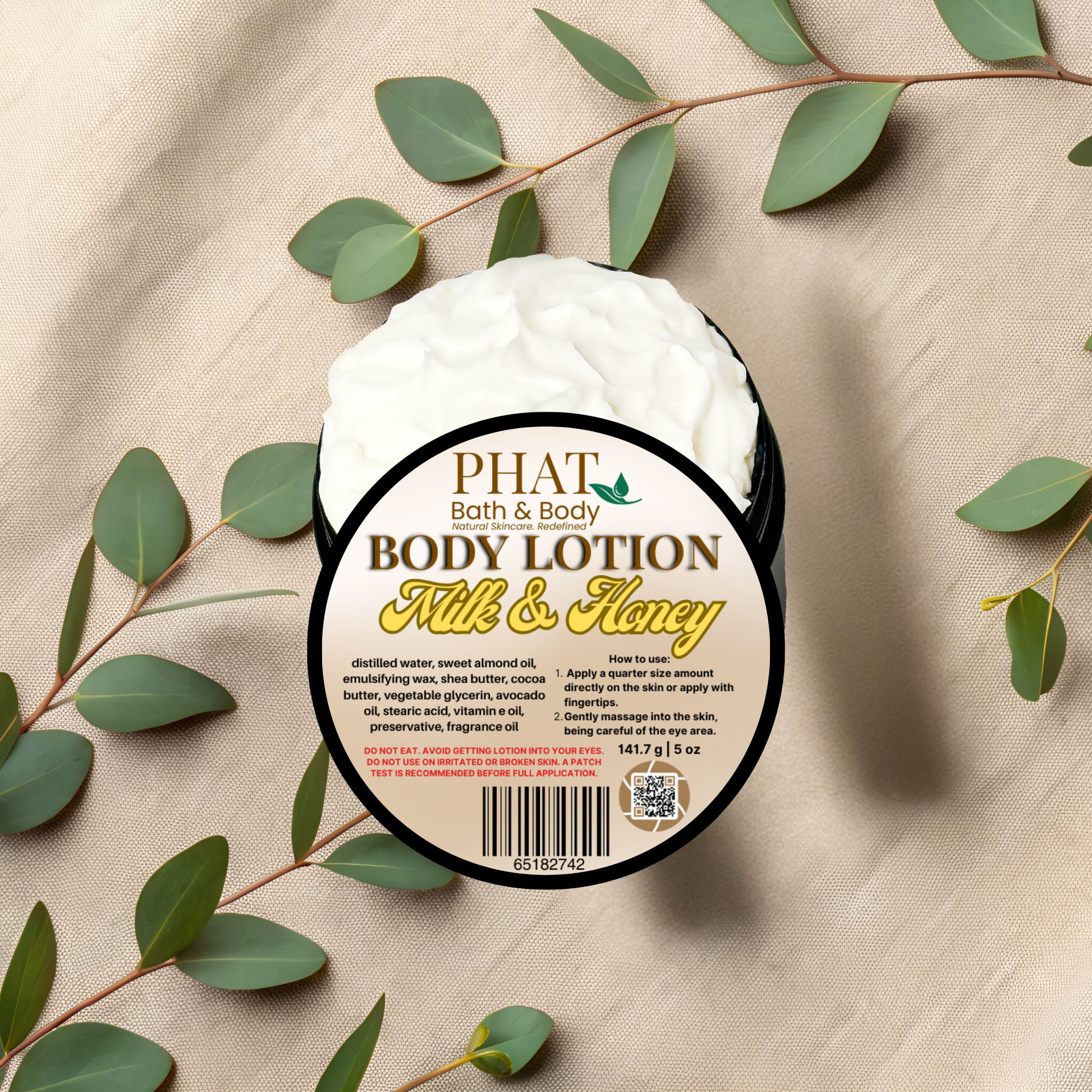 Body lotion container labeled 'Milk & Honey' by Phat Bath & Body on a beige fabric background with green leaves.