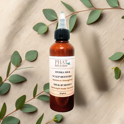 An amber twist top bottle of PHAT Bath & Body Scalp Restore Milk & Honey scalp treatment, styled on a beige fabric background with eucalyptus leaves.