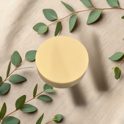 Round yellow soap bar on a beige fabric background with green leaves