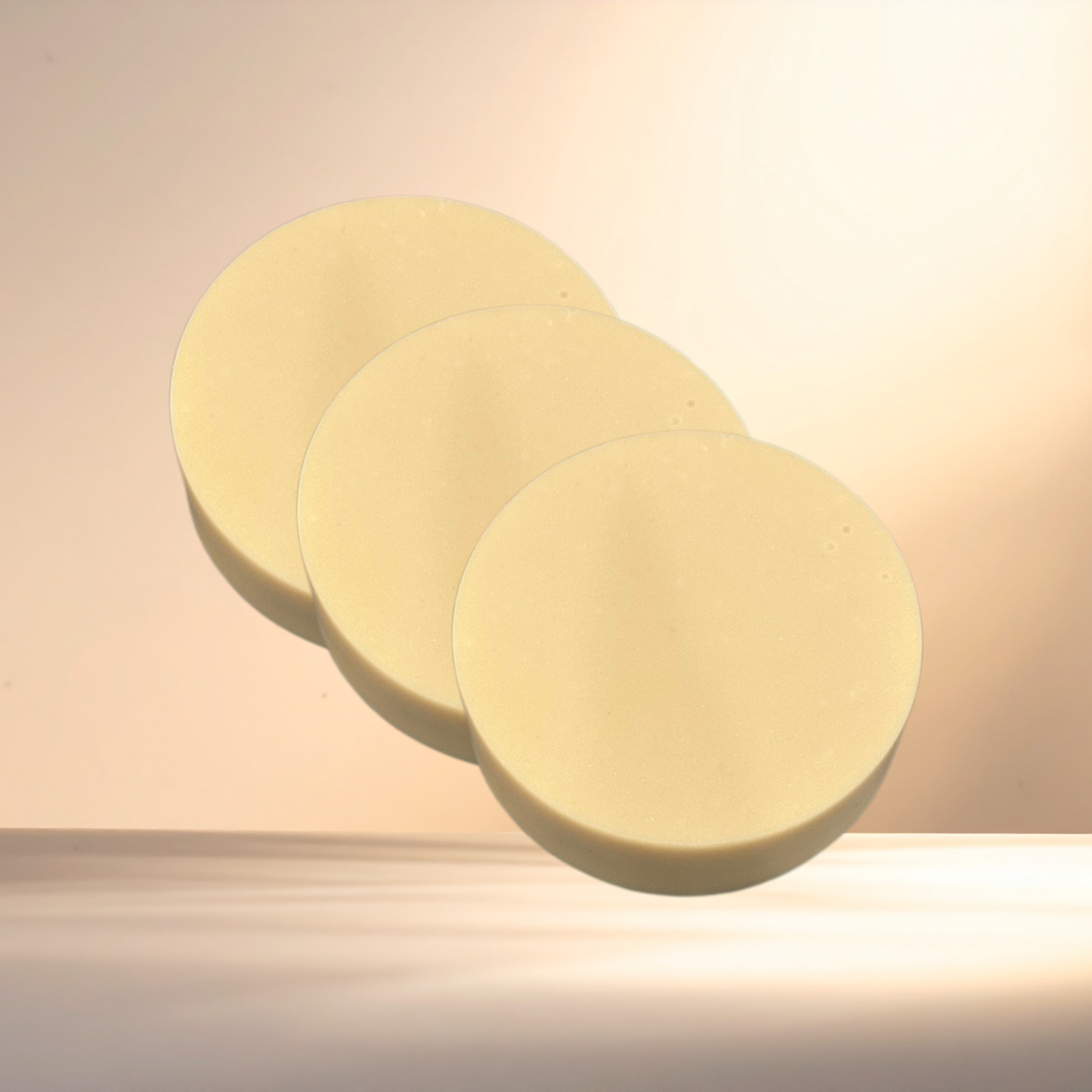 Three round, light-colored soaps on a beige surface with a soft focus background.