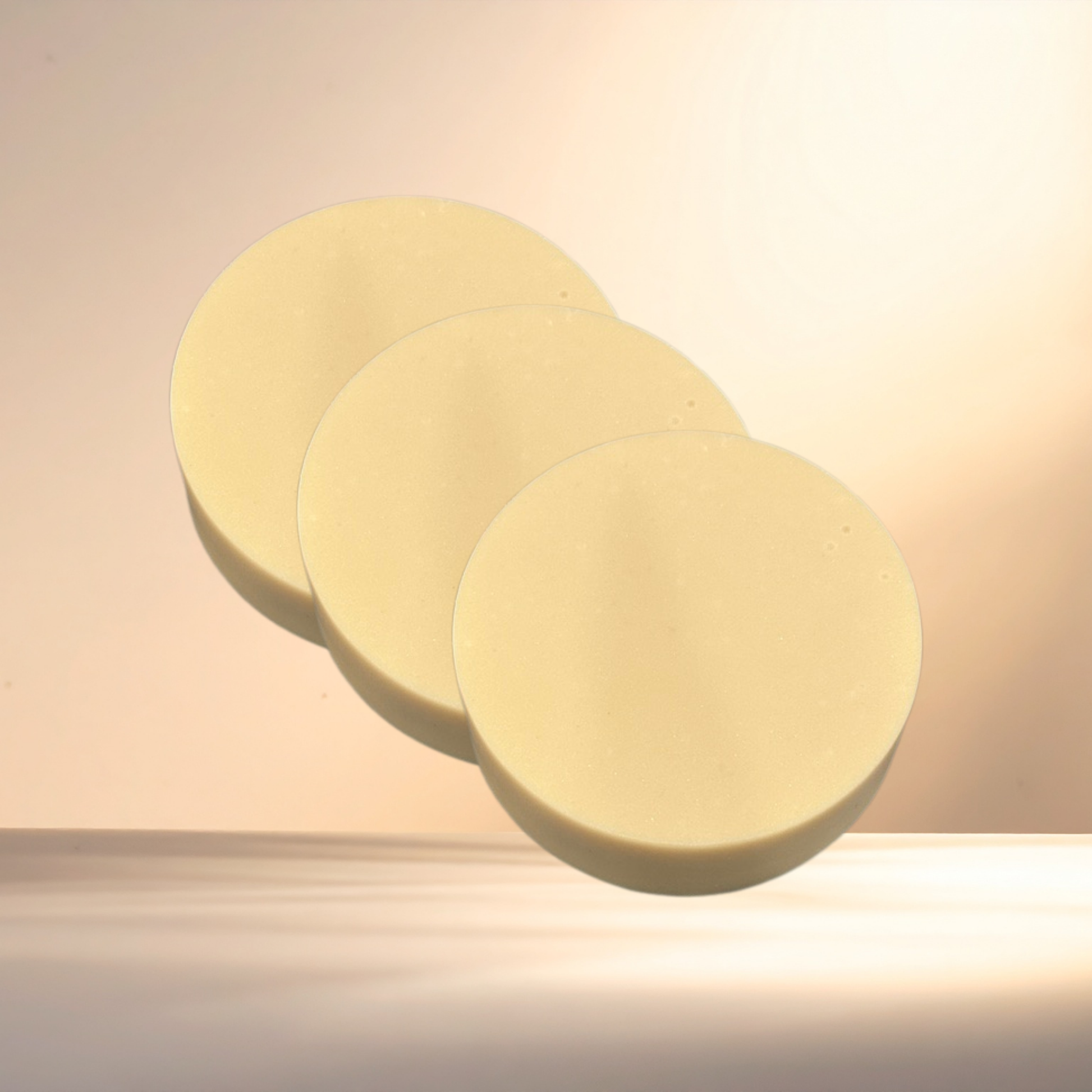 Three round, light-colored soaps on a beige surface with a soft focus background.