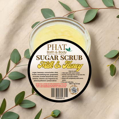 Jar of Phat Bath & Body Sugar Scrub with a label on a beige fabric background with green leaves.
