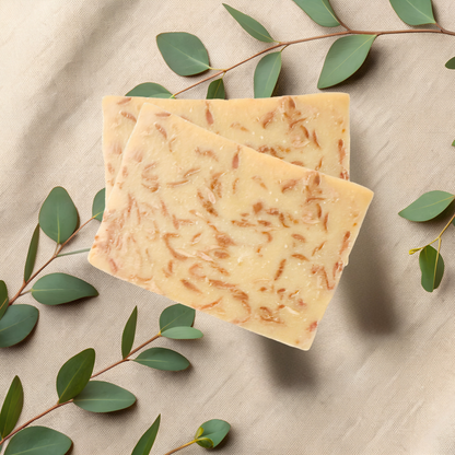 Two bars of soap with natural texture on a beige fabric background with green leaves.