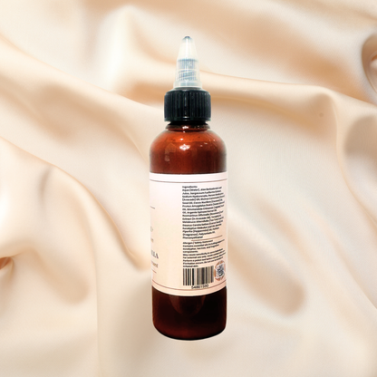 An amber dropper bottle with a black twist cap and a cream-colored label, shown from the back against a draped beige satin fabric background.