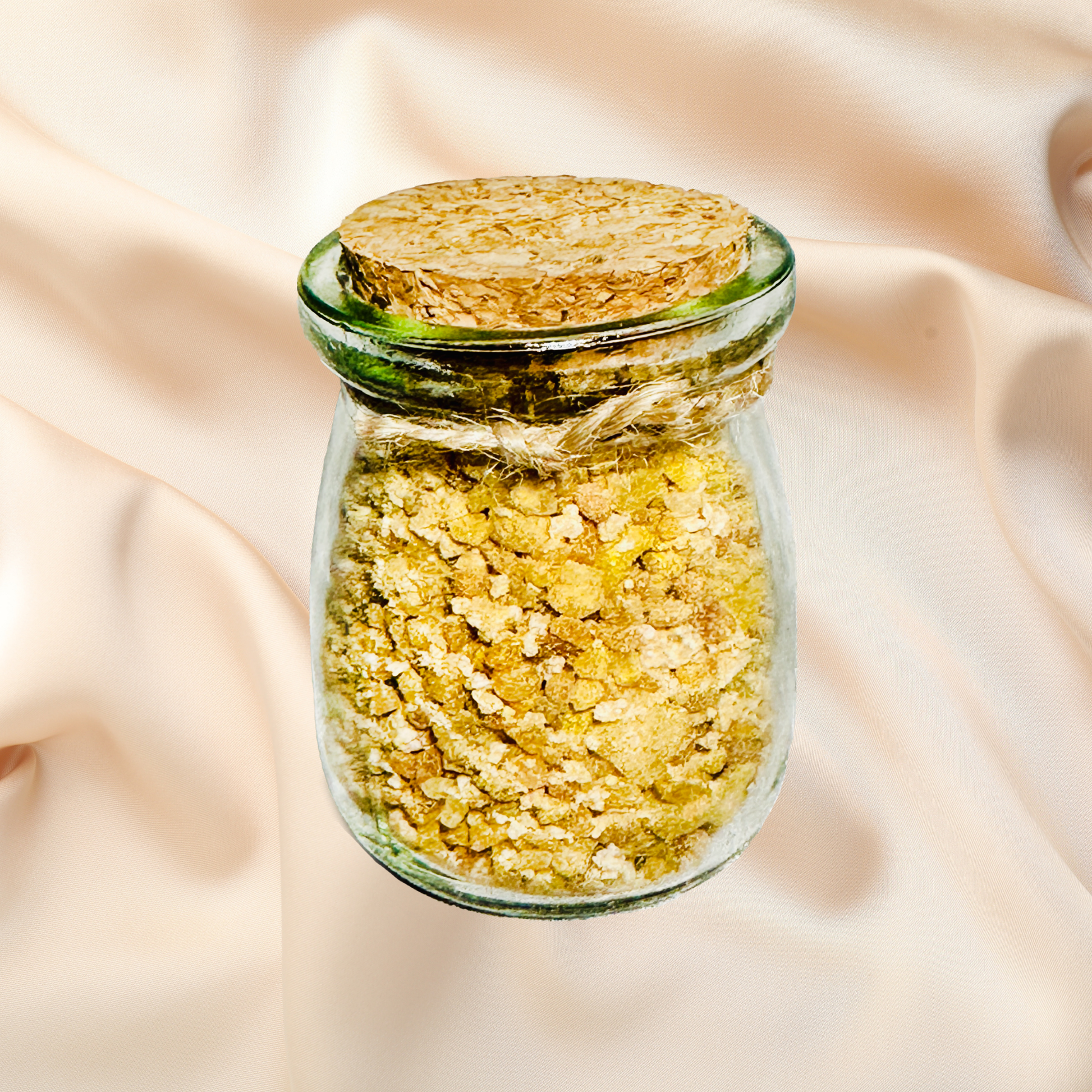 Glass jar with cork lid containing yellow bath salts on a beige fabric background