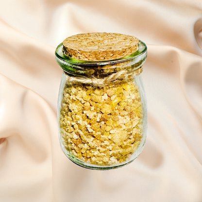 Glass jar with cork lid containing yellow bath salts on a beige fabric background