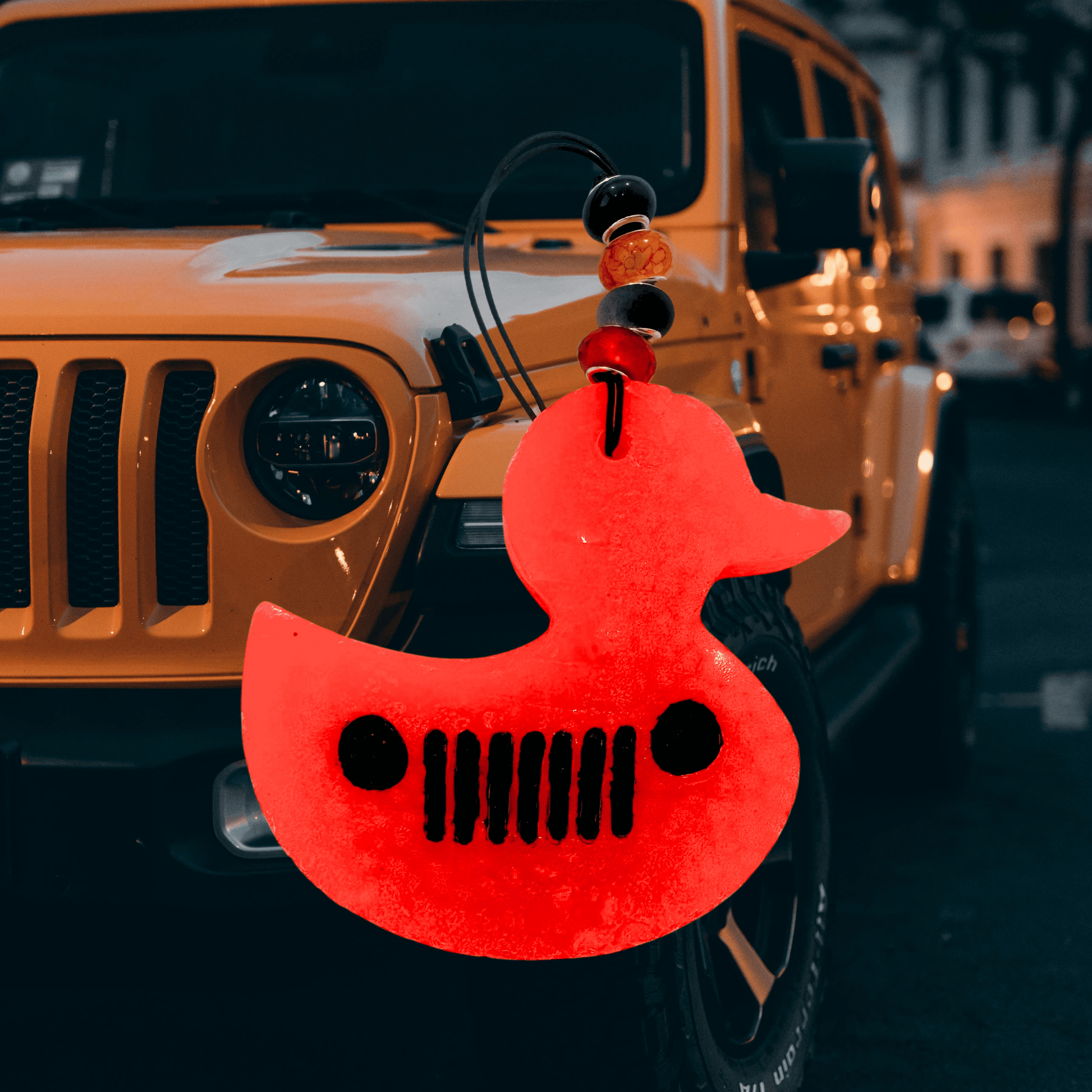 Red rubber duck shaped like a car grille in front of an orange Jeep Wrangler.