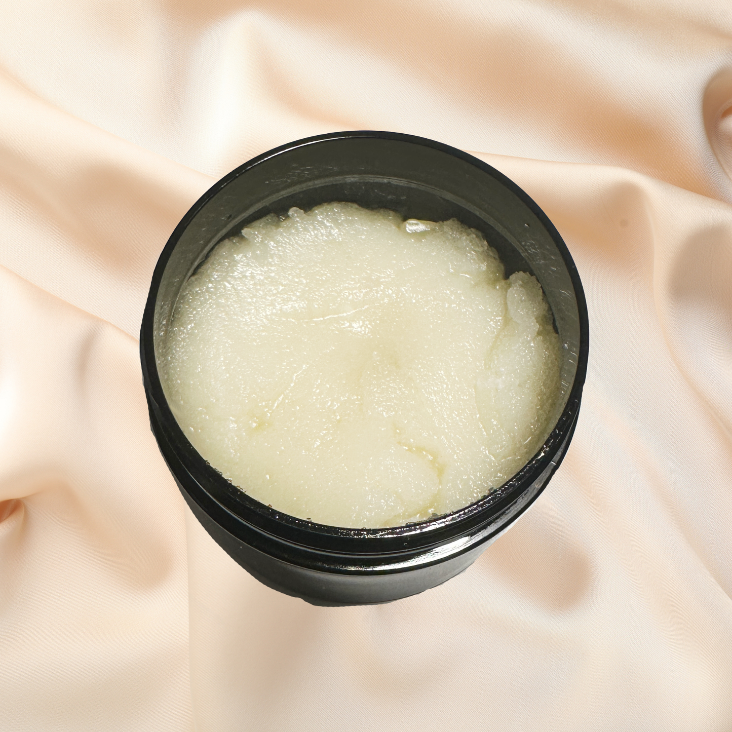 Black container of white scrub on a soft pink fabric background