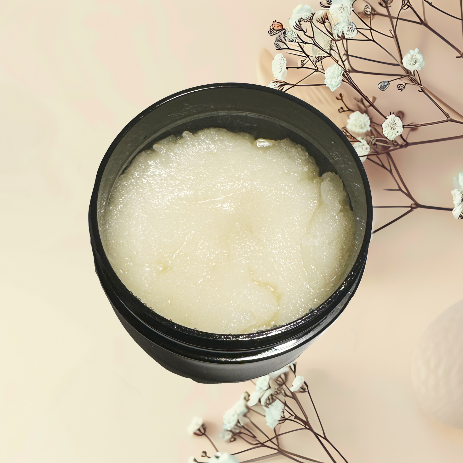 Black container of white scrub with dried flowers on a beige background