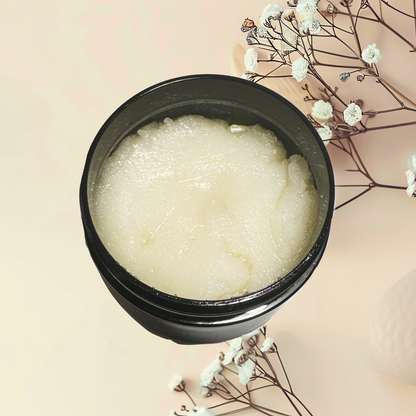 Black container of white scrub with dried flowers on a beige background