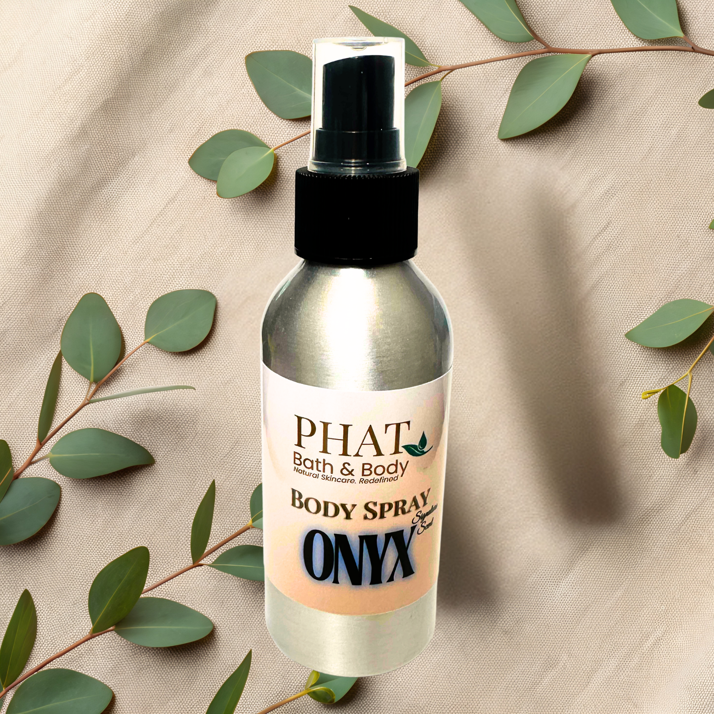 Body spray bottle labeled 'PHAT Bath & Body' on a beige fabric background with green leaves.