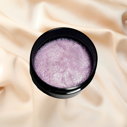 Black container with purple sugar scrub on a beige fabric background